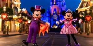 Mickey and Minnie Mouse in festive costumes pose cheerfully in an empty street, illuminated by colorful lights and a castle in the background.