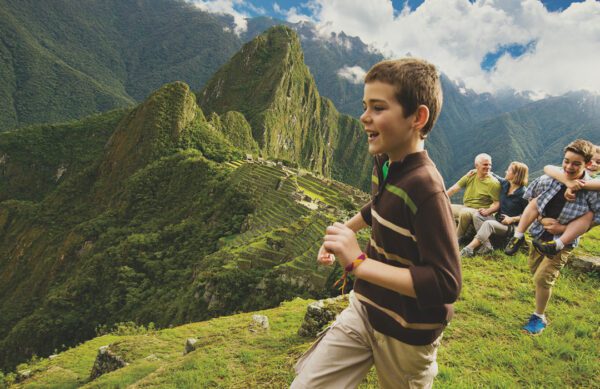 content 3-abd A boy laughs and runs in front of a lush green landscape with mountains, while others sit in the background, enjoying the view.