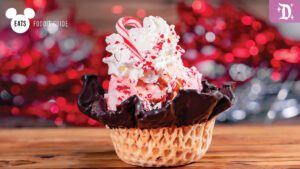 A festive ice cream sundae topped with whipped cream, candy cane pieces, in a chocolate-dipped waffle bowl, set against a vibrant background.