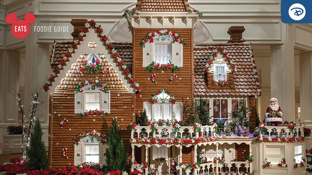 A large, intricately decorated gingerbread house featuring festive details, surrounded by vibrant greenery and holiday decorations.