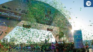 Celebratory confetti rains down at the finish line of a Disney event, with a vibrant arch and cheering crowd in the background.