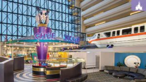 Interior view of a colorful atrium featuring a whimsical display with a cow statue, a monorail, and modern seating areas.