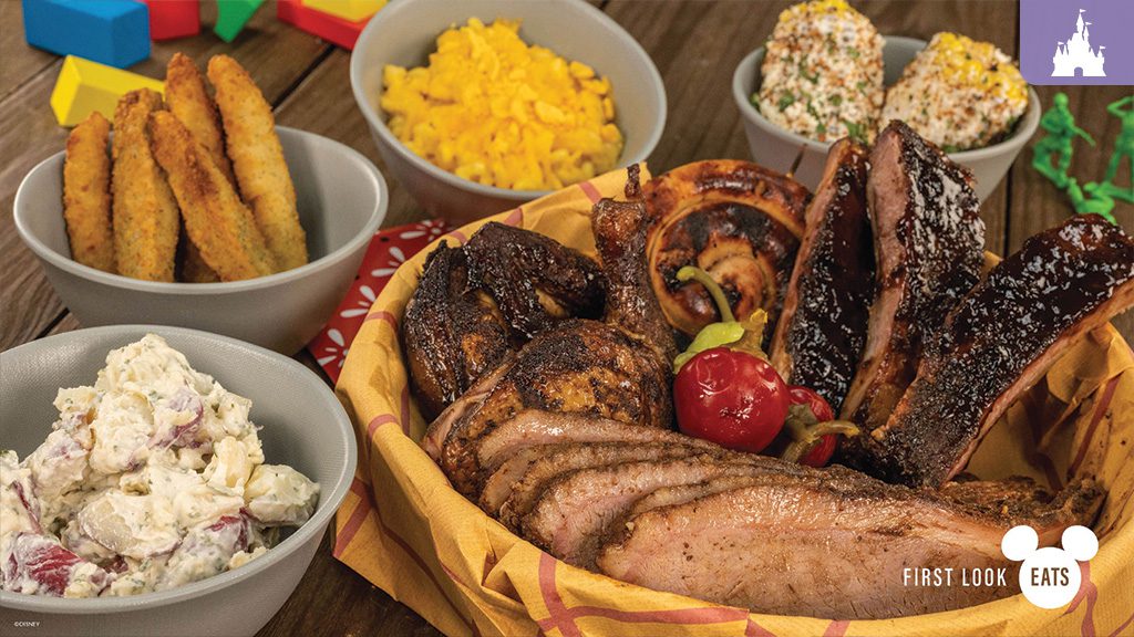 A basket filled with grilled meats, a cherry on top, surrounded by bowls of mac and cheese, potato salad, and cornbread.