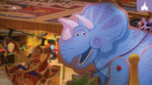A colorful, cartoonish blue triceratops with a big smile stands in a playful setting, surrounded by playful decor and vibrant characters.