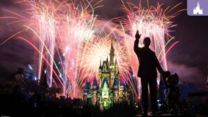 A silhouette of a person stands beside a statue, overlooking a castle illuminated by vibrant fireworks in the night sky.