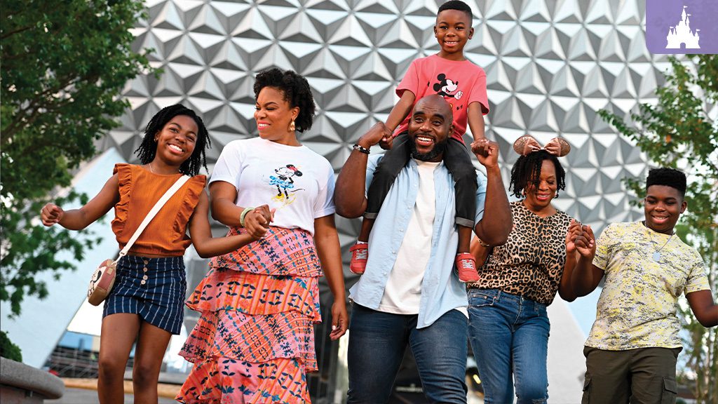 A joyful family of five walks together, smiling, in front of a futuristic building, with trees and greenery around them.