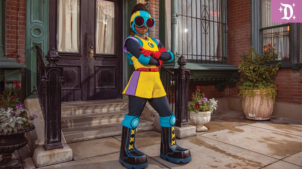 A colorful, futuristic character stands confidently on a sidewalk, wearing a vibrant outfit with oversized sunglasses, in front of a brick building.