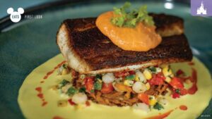 A beautifully presented plate featuring a piece of grilled fish on a bed of colorful vegetables and a creamy sauce, topped with a dollop of sauce.
