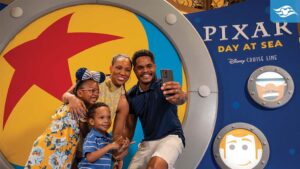 A family of four poses for a selfie in front of a colorful Pixar-themed backdrop, smiling and enjoying a fun moment together.