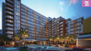 Modern multi-story hotel with large windows, surrounded by palm trees and a pool area, set against a twilight sky.