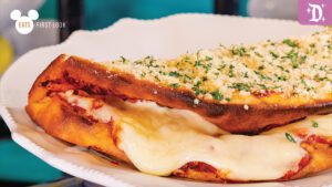 A close-up of a cheesy, garlic-topped bread dish, featuring melted cheese and a golden-brown crust, served on a white plate.