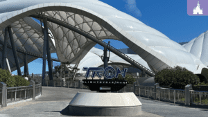 A futuristic entrance with the "TRON Lightcycle Run" sign underneath a sleek, white, curved structure against a blue sky.