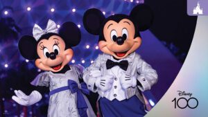 Mickey and Minnie Mouse in elegant attire, smiling against a colorful, festive background, celebrating Disney's 100th anniversary.