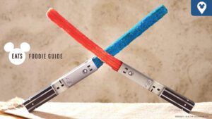 Two colorful lightsaber-style treats, one red and one blue, cross over a sandy background. Text reads "EATS FOODIE GUIDE."