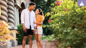 A couple enjoys a moment together in a lush garden, surrounded by vibrant flowers, smiling and looking at each other affectionately.
