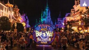 A vibrant nighttime scene of a Halloween parade at a theme park, featuring colorful lights and a crowd enjoying the festivities.