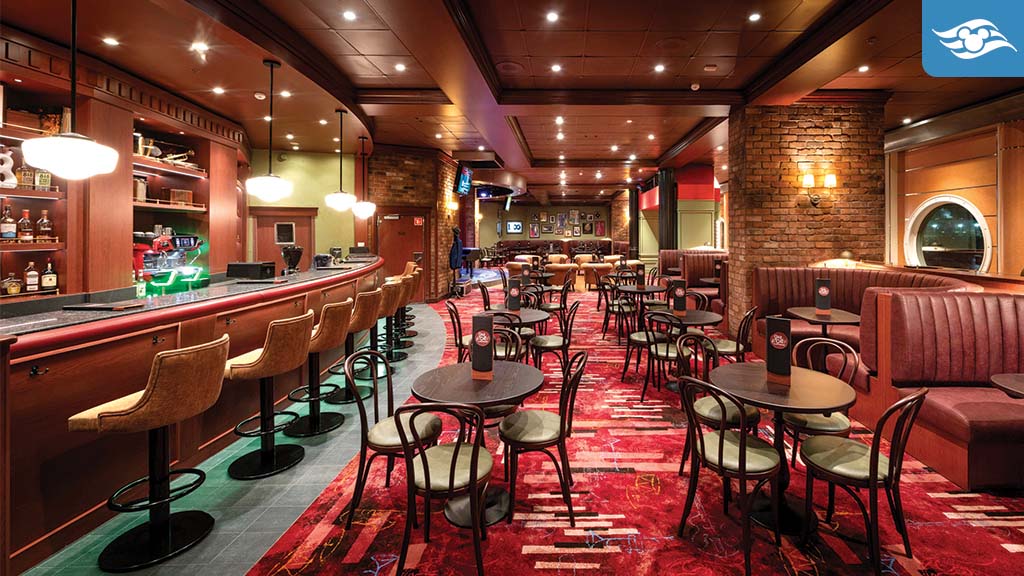 A cozy bar interior with wooden furnishings, circular tables, and soft lighting. A long bar is lined with stools, creating a warm atmosphere.