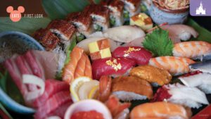 A vibrant sushi platter featuring various sushi types, sashimi, and colorful garnishes arranged on a green leaf background.
