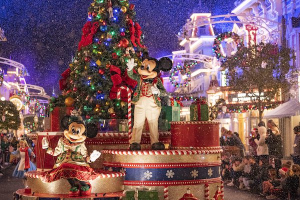 Mickey Mouse and a friend celebrate the holidays on a festive float, surrounded by colorful decorations and snow in a cheerful atmosphere.