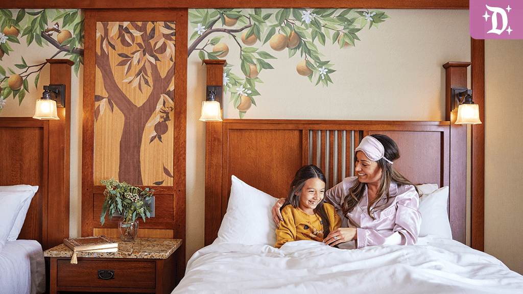 disney-visa-cardmember-discount-disneyland A mother and daughter cuddle in bed, surrounded by warm decor and a mural of a tree, creating a cozy, inviting atmosphere.