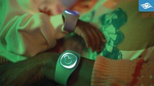 Close-up of a parent and baby's wrists wearing glowing wristbands in a softly lit environment, showcasing a connection between them.