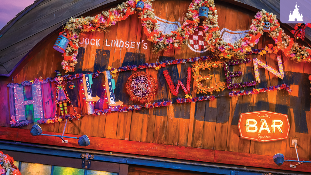 Wooden bar facade reading Jock Lindsey’s HALLOWEEN BAR, decorated with autumn garlands, a small scarecrow figure and a glowing neon BAR sign