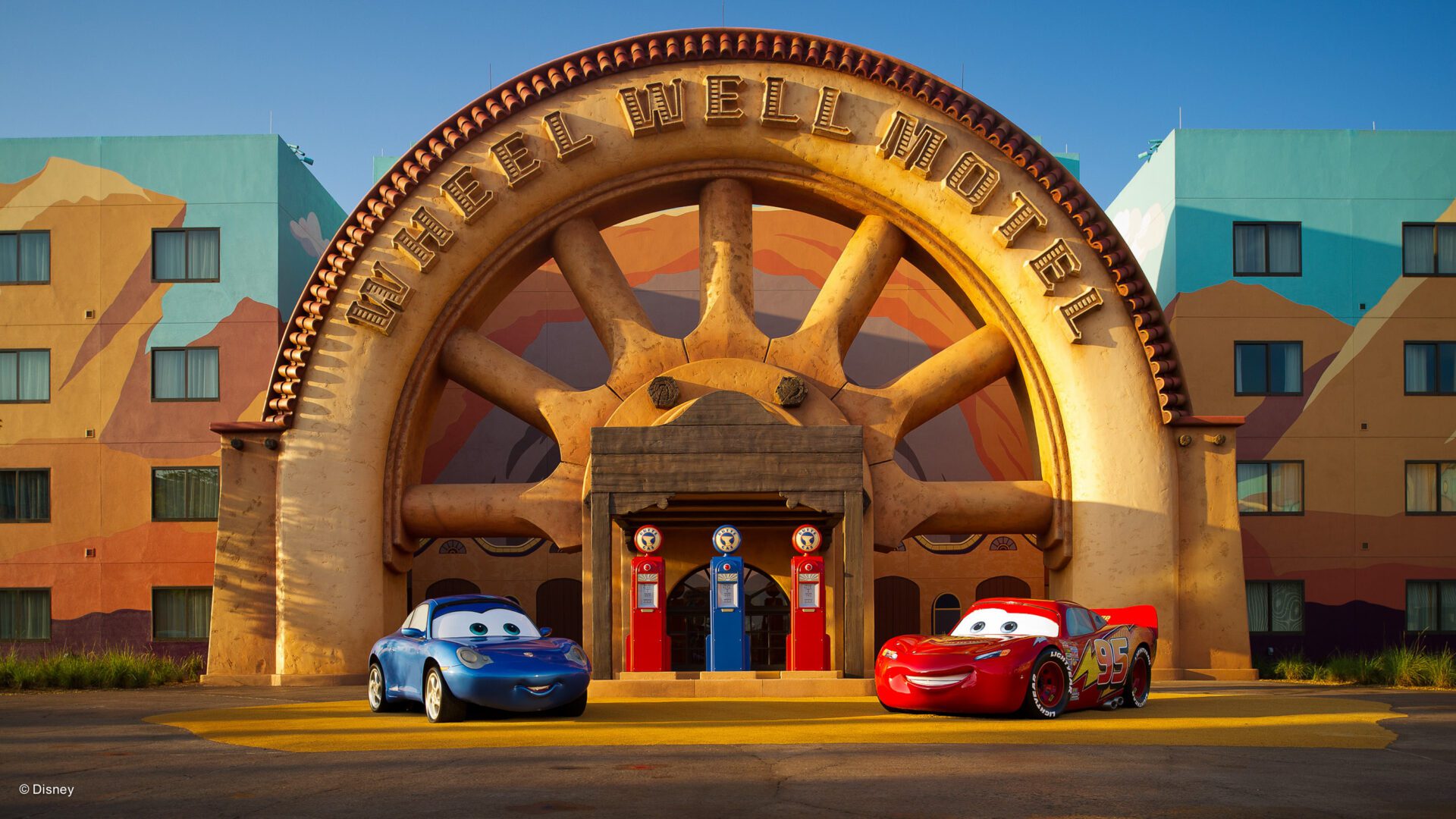 A colorful hotel entrance shaped like a giant wheel, with two animated cars, one blue and one red, parked outside.