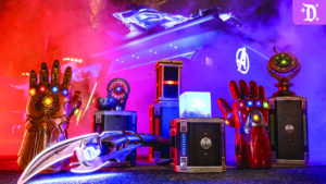 Colorful display of Marvel-themed props, including glowing gauntlets and futuristic devices, surrounded by mist and vibrant lights.