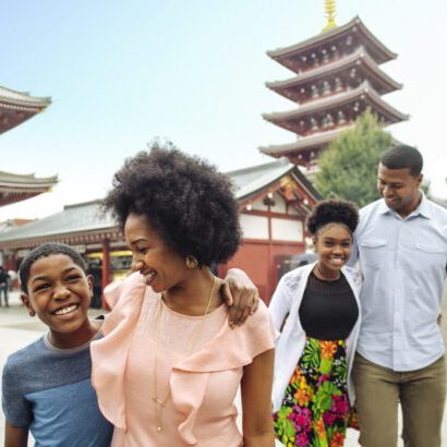 A joyful family walks together outdoors, smiling. Traditional Asian architecture is visible in the background, adding cultural context.