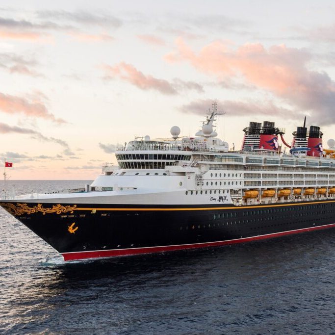 Disney Copyright Imagine Disney Cruise Line Ship A large cruise ship with a black hull, red accents, and multiple decks sails through calm ocean waters under a colorful sunset sky.