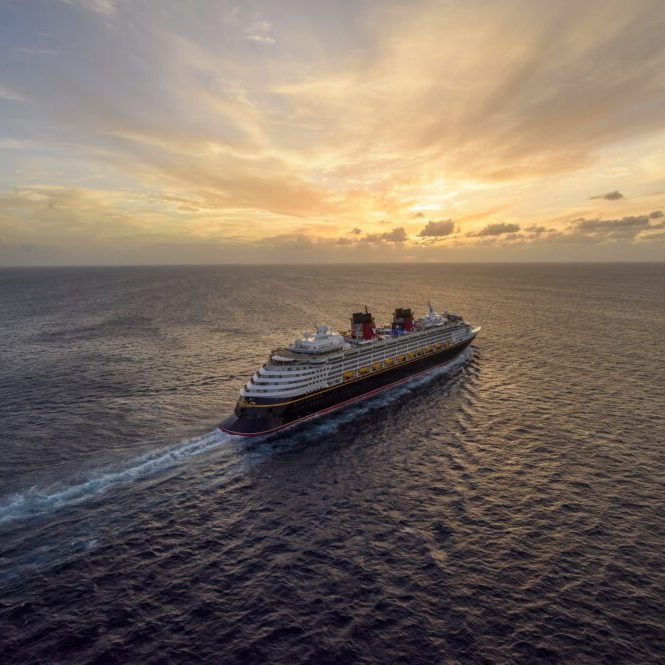 A cruise ship glides across the ocean at sunset, leaving a trail in the water under a colorful sky.
