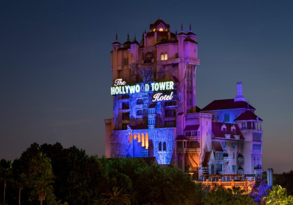DisneysHollywoodStudiosTowerofTerror The Hollywood Tower Hotel at dusk, illuminated in purple and blue lights, featuring a vintage hotel design and a prominent sign.