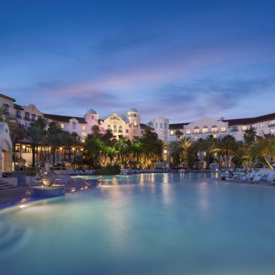 A tranquil resort scene at dusk, featuring a serene pool surrounded by palm trees and elegant buildings in the background.