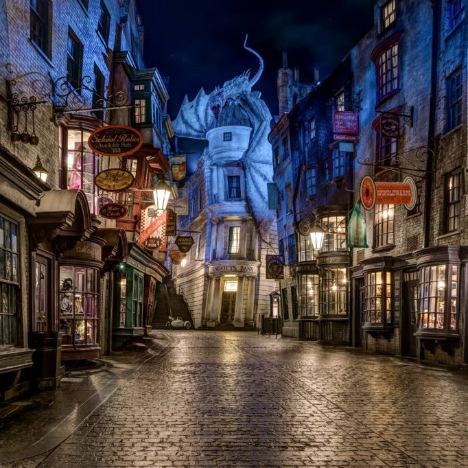 A dimly lit, cobblestone street lined with charming shops and illuminated signs, set at night, exuding a magical atmosphere.