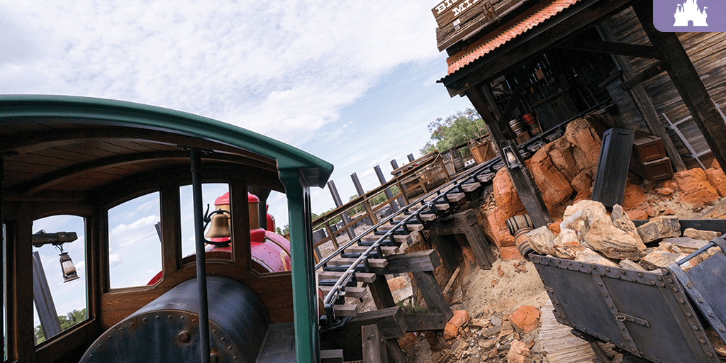 Thunder Mountain Railroad train on the track at Magic Kingdom, passing rustic mining structures and rocky terrain at Disney World
