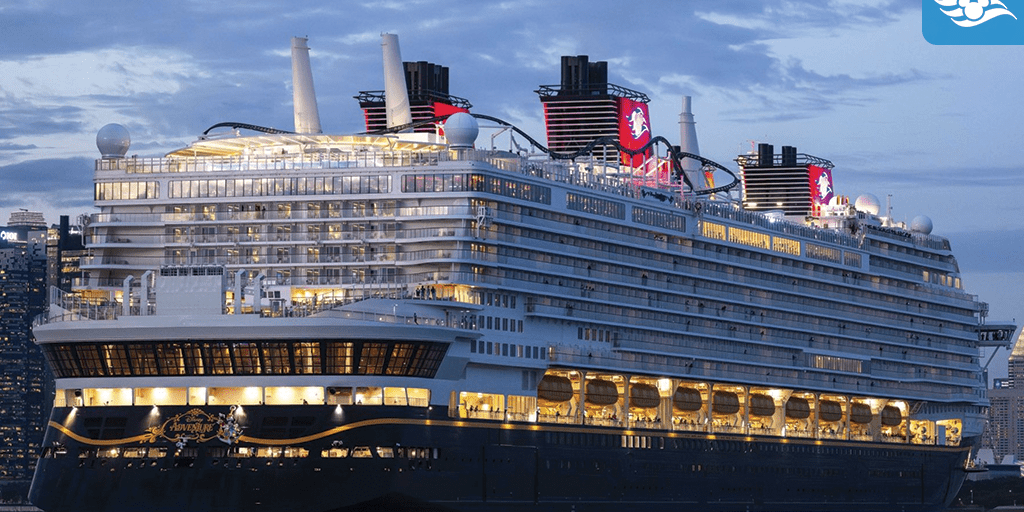 Disney Adventure cruise ship docked at dusk with glowing decks and onboard roller coaster visible above the skyline in Singapore.
