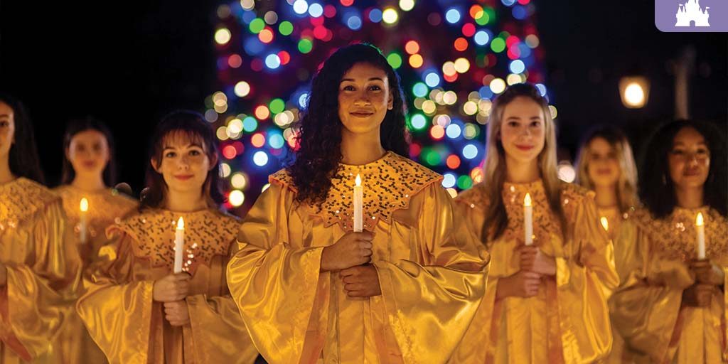 Choir members in golden robes holding candles in front of a brightly lit Christmas tree at EPCOT’s Candlelight Processional.
