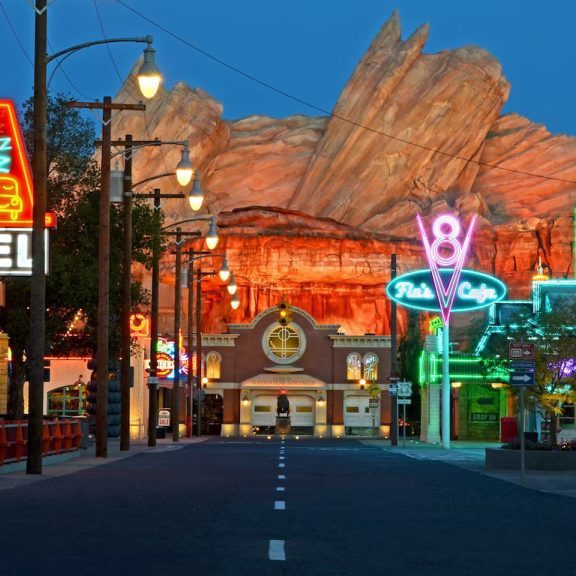 A vibrant, neon-lit street scene featuring vintage signs, a motel, and rocky mountains under a twilight sky.