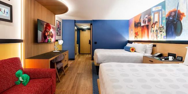 Modern hotel room featuring two beds, colorful walls with character artwork, a TV, and a cozy red sofa.