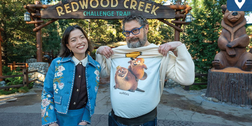 Two guests pose under the Redwood Creek Challenge Trail sign at Disney California Adventure, showing a Pixar Hoppers character T-shirt.