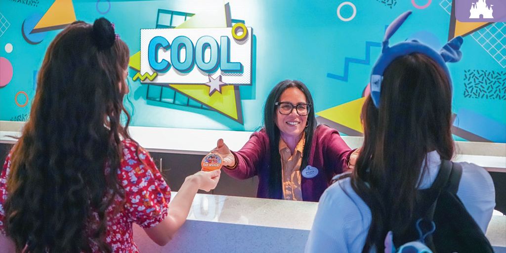 Disney cast member greeting guests at Pop Century Resort check-in desk with colorful retro “cool” wall design in background