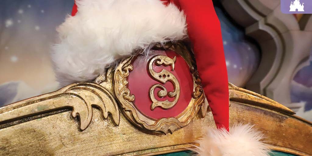 Santa hat resting on an ornate gold chair with a red "S" emblem, set against a festive Disney backdrop.