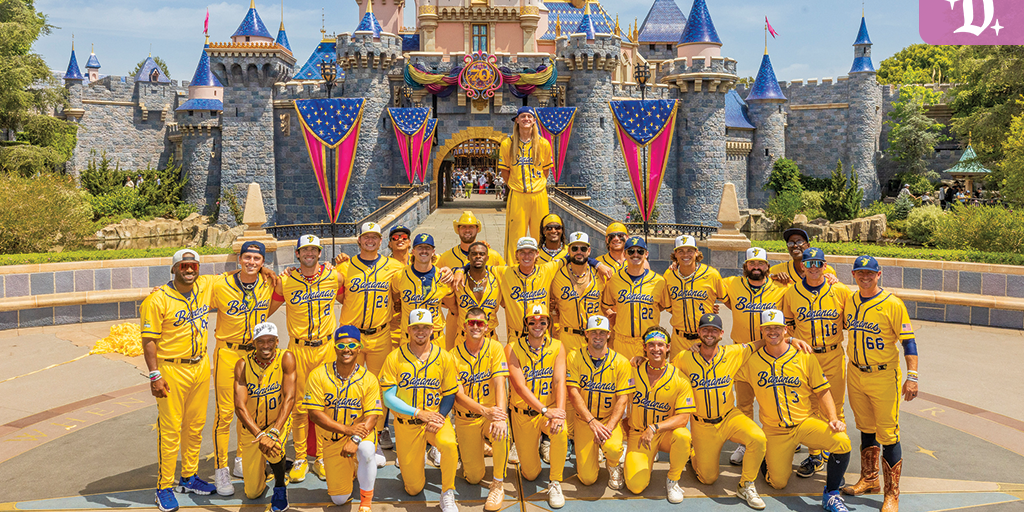 The Savannah Bananas baseball team poses in bright yellow uniforms in front of Sleeping Beauty Castle at Disneyland, with festive red, white, and blue decorations.