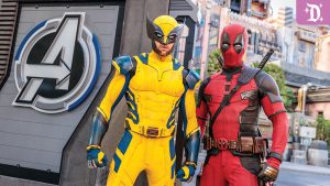 Two superheroes stand together: one in a yellow and blue costume (Wolverine) and the other in a red outfit (Deadpool), with an Avengers logo in the background.