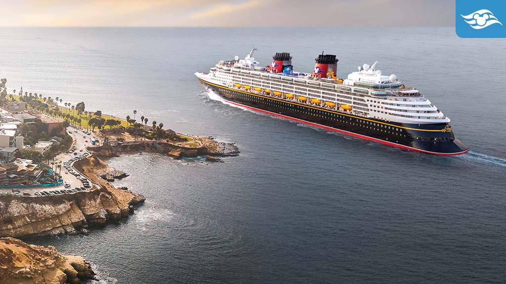 disney-cruise-line-additional-2026-itineraries Disney Cruise ship sailing past the scenic coastline of San Diego at sunset, with La Jolla cliffs and palm trees visible.