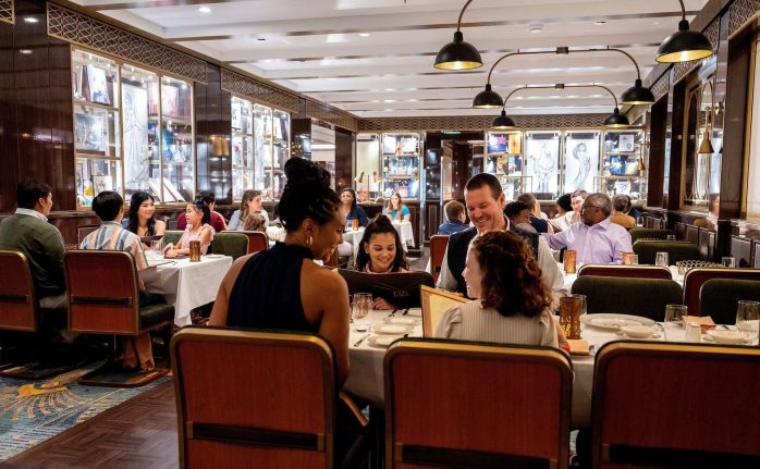 A bustling restaurant scene with diners at elegantly set tables, enjoying meals and conversations in a warm, stylish atmosphere.