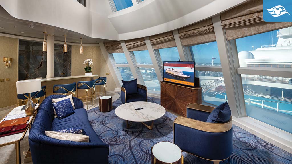 disney-cruise-line-fantasy-updates Luxurious two-story Disney Fantasy Tower Suite with floor-to-ceiling windows, plush navy seating, marble table, and elegant bar area.