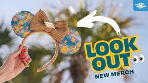A hand holds a pair of colorful mouse ear headbands adorned with a bow, with text promoting new merchandise in the background.