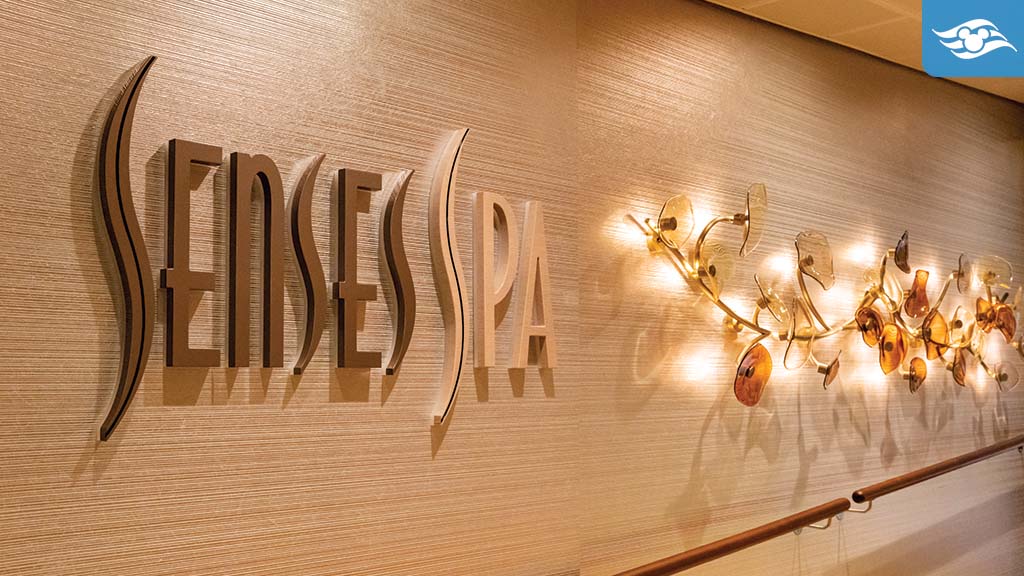 disney-cruise-line-senses-spa-treatments The interior of a spa featuring the sign "SENSES SPA" on a textured wall, accompanied by soft, ambient lighting and decorative elements.