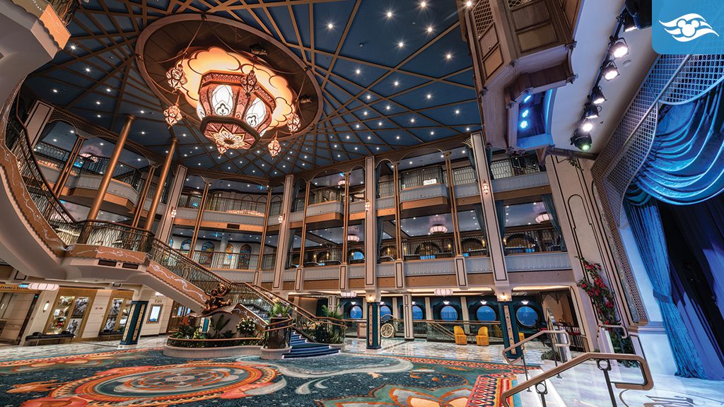 disney-cruise-line-treasure-grand-hall The Grand Hall aboard the Disney Treasure, featuring a majestic bronze statue of Aladdin, Jasmine, and the Magic Carpet, elegant staircases, intricate carpets with detailed patterns, and a grand chandelier inspired by Aladdin.